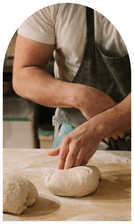 Man wearing an apron and white t-shirt kneading dough on a wooden surface